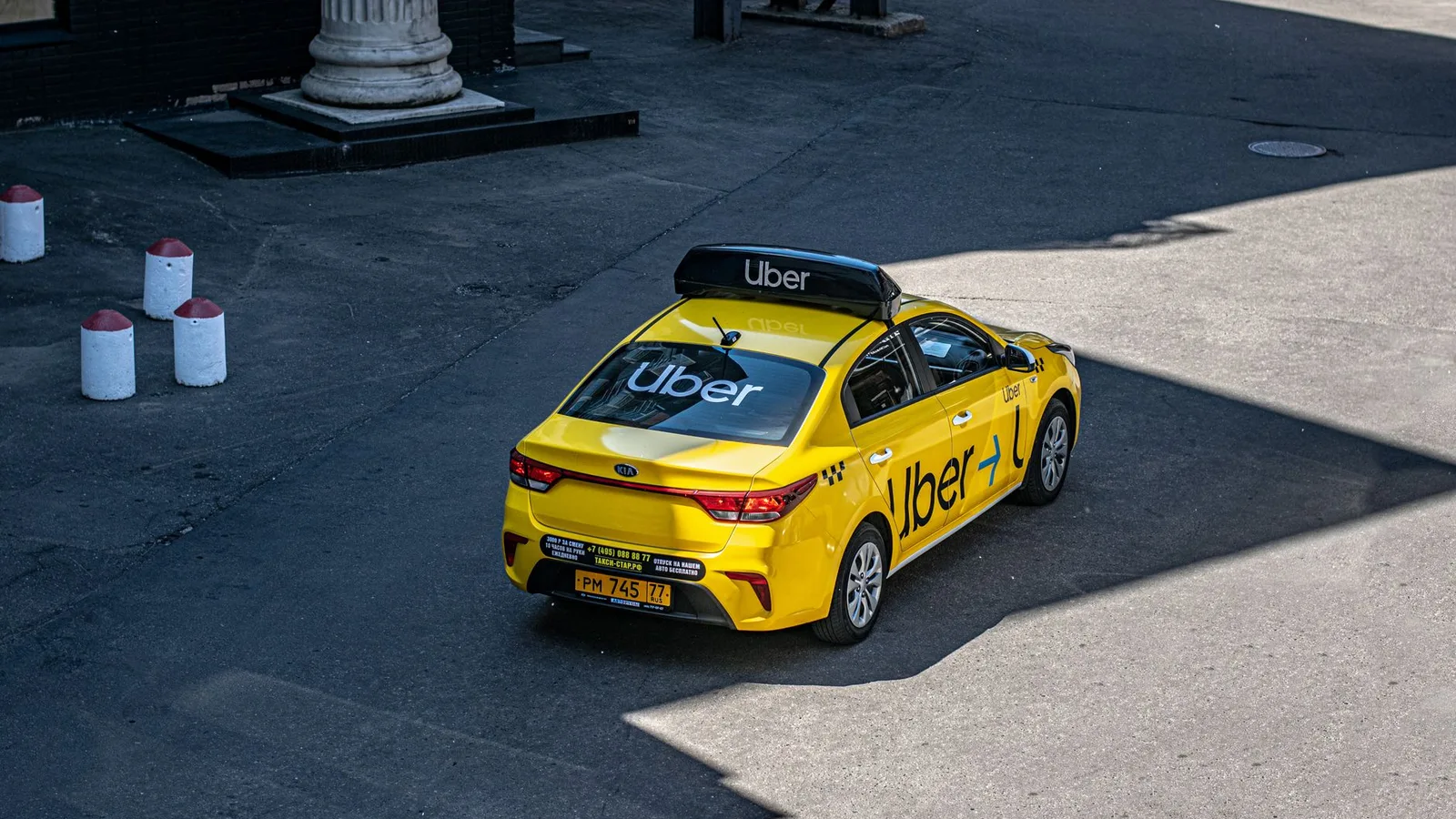 A yellow Uber taxi driving on a city street, shown from above.