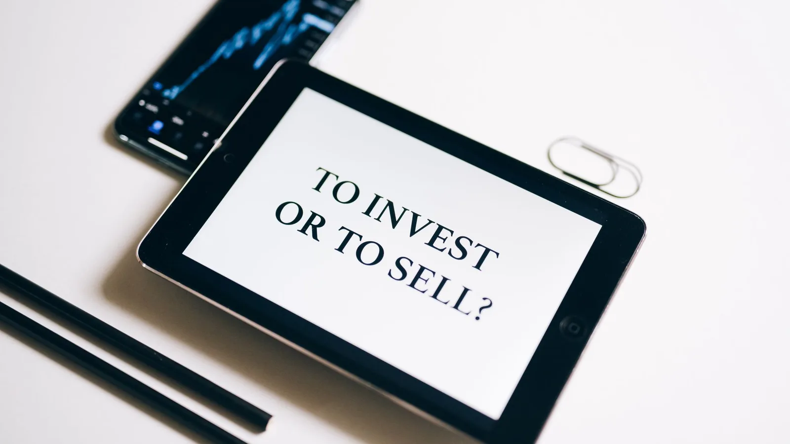 A tablet with text 'To Invest or To Sell?' on a white background.
