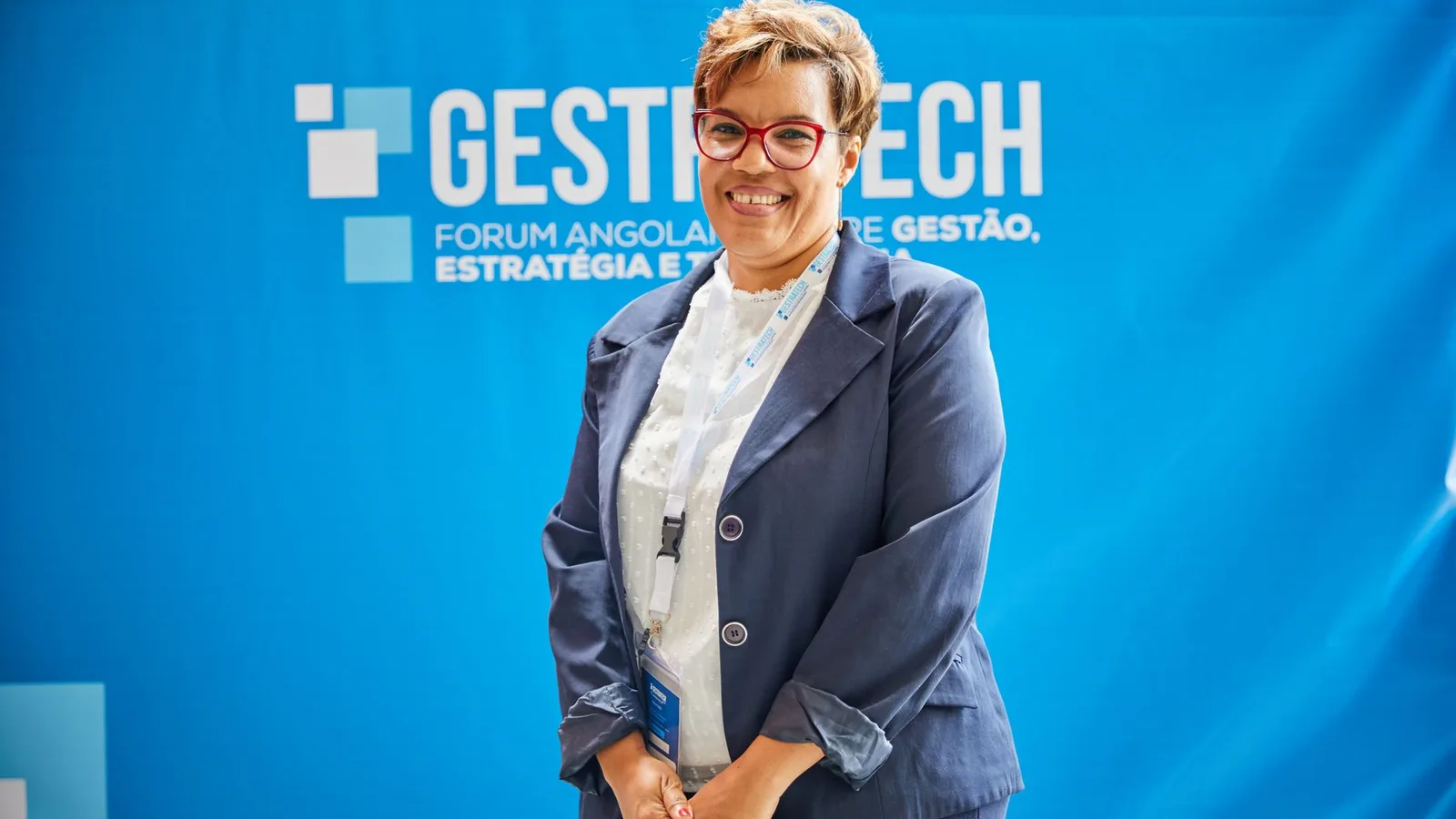 Businesswoman smiling in front of blue backdrop at trade fair event, embodying leadership and professionalism.