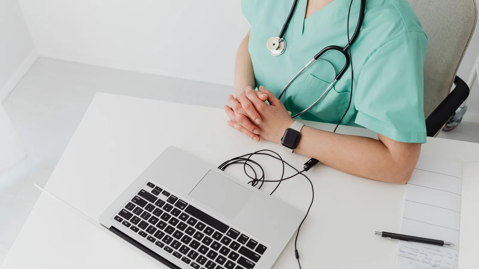 Doctor in scrubs with stethoscope conducting online consultation using a laptop.