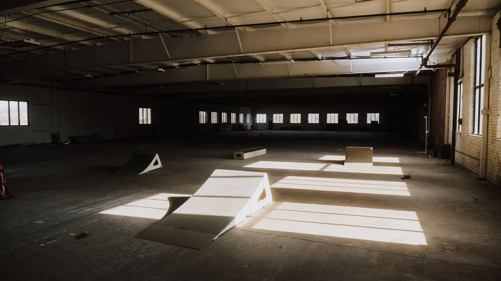 Sunlight casting shadows over ramps in an empty indoor skate park.