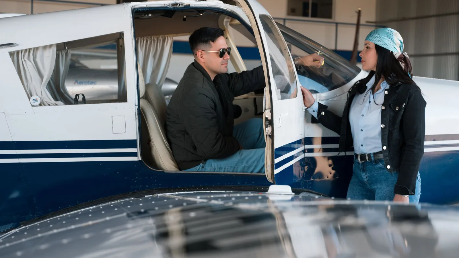 Two adults preparing a small plane for flight inside a hangar.