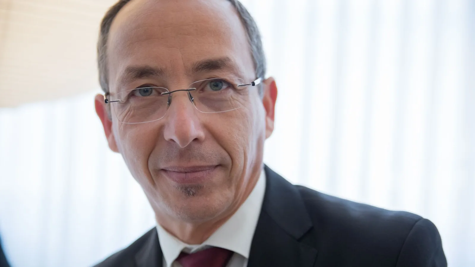 Close-up of a well-dressed businessman wearing glasses, smiling confidently indoors.